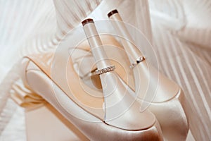 Silver wedding engagement rings on heels of bride shoes with dress in the background