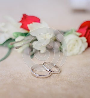 Silver wedding rings lie before boutonnieres