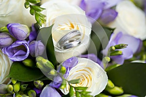 Silver wedding rings on wedding bouquet of white and violet flowers
