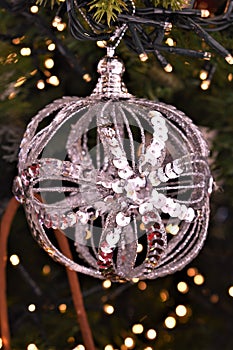 Silver white sparkling ornament hanging from greenery and surrounded by lights.