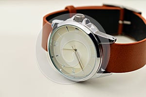 Silver wrist watch with a brown double-sided single-piece leather strap. Zulu or nato strap. White background