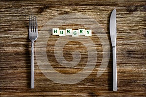 Silverware set on wooden table with sign Hungry