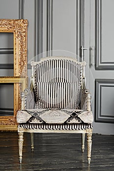 Silvery armchair and golden frames in room with photo