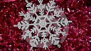 A silvery snowflake lies on New Year`s red tinsel and slowly moves clockwise. Christmas winter background. Happy New Year 2021