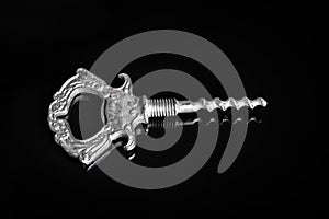 Silvery vintage corkscrew in the form of a key on a black background