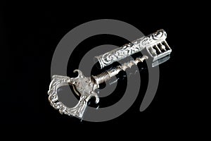 Silvery vintage corkscrew in the form of a key on a black background