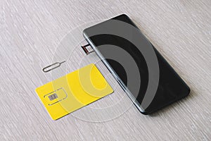 SIM card and microSD card tray with removal tool at the side of smartphone on wooden table. free space for design and