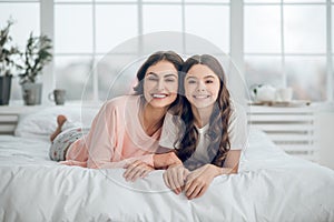Similar mom and daughter lying on stomachs on bed