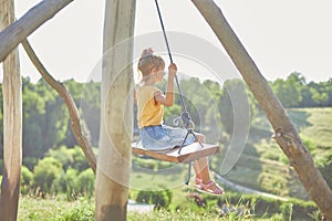 Similing little girl swinging on a large rustic wooden swing in the park, sunlight