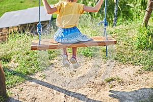 Similing little girl swinging on a large rustic wooden swing in the park, sunlight