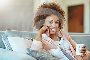 Simmering down with a cup of tea. Portrait of a young woman relaxing with a warm beverage at home.