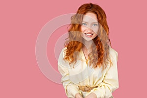 Simpathic redhead young woman with blue eyes posing for the camera with happy facial expression on pink background and