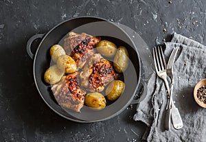 Simple baked chicken with new potatoes in a cast iron pan on dark background, top view.