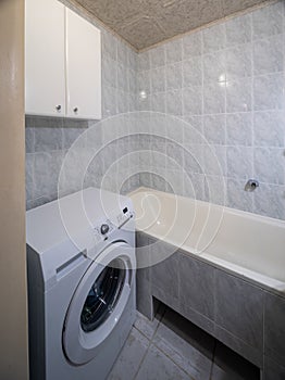 Simple bathroom interior in modern apartment. White bath and tile. Washing machine