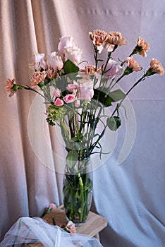 simple bouquet of springtime flowers on glass pot with natural light. vertical image. roses  carnation  gillyflower  daisy. jute