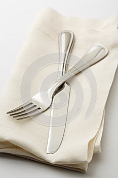 Simple, casual fine dining place setting with high quality silverware fork and knife on white linen napkin with white tablecloth