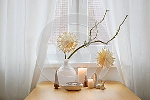 Simple Christmas decoration with two paper stars hanging on bare branches, candles and small natural objects on a table by the