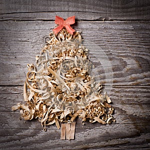 Simple Christmas tree arranged from sawdust, wood-chips on wooden background. Orange cute ribbon.