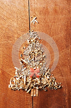 Simple Christmas tree arranged from sawdust, wood-chips on wooden background. Orange cute ribbon