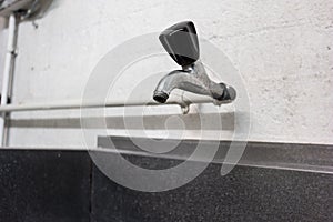 Simple chromed metal cold water faucet and connecting pipes over a metal sink inside a common use laundry room