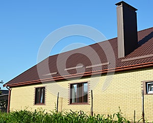 A simple construction brick house with brown metal roof, snow-guards and chimney against blue sky