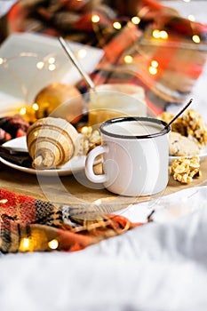 Simple country home breakfast in bed, coffee with milk and homemade pastry on plaid blanket