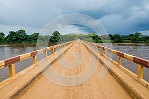 Simple dirt road bridge over tropical river with dramatic clouds in Republic of Congo, Africa