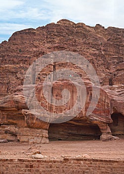 Simple dwelling ruins - cave like holes in stone wall, Jordan flag waves on top, typical Petra scenery