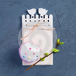 Simple Easter holiday composition of decorated cupcake, branch with young shoots of greenery and handcraft notebook with empy blan