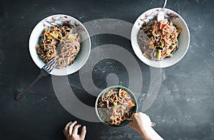 Simple family dinner, buckwheat vegan noodles with vegetables and beans, three plates and forks, child hands, top view