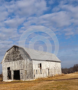 Simple Greying Barn Sits on Field Against Backdrop of Sky, Clouds, and Golden Ground photo
