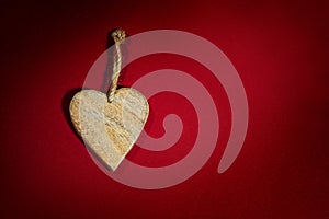 Simple heart shape made of wood with a rustic cord on a background of dark red felt, holiday greeting card and love symbol for