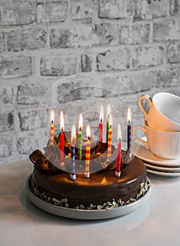 Simple homemade chocolate birthday cake with burning candles on the table. Holiday concept