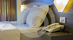 Simple hotel room interior with one bed, two pillows and telephone