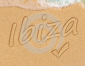 Simple Ibiza Spanish holiday getaway message written in smooth sand with an incoming wave on a tropical beach