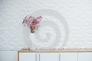 Simple interior of room with white textured walls and flowers on the table