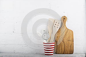 A simple kitchen still life against a white brick wall: cutting board, cooking equipment, ceramics. Horizontal