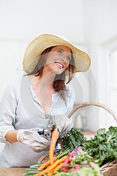 The simple life. A gorgeous woman, wearing a straw hat, cuts the stems off fresh vegetables in a basket on the kitchen