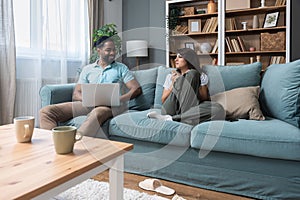 Simple living. Happy young couple husband and wife sitting relaxed on couch in living room reading book drinking tea together,