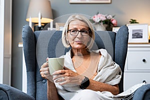 Simple living. Senior woman sitting alone on chair at home drinking tea or coffee enjoying her time and life. Older female