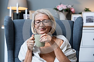 Simple living. Senior woman sitting alone on chair at home drinking tea or coffee enjoying her time and life. Older female