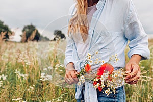 Simple living. Woman holding bouquet of wildflowers with red poppies wearing linen shirt in meadow. Enjoying nature