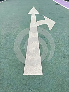 Simple make a turn choice concept: White isolated arrow on green pavement showing direction straight ahead or right