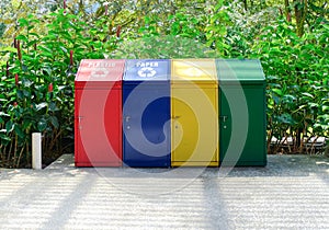 Simple metal recycling bins in bright colours for trash sorting. For mockup purpose. Plants in background.