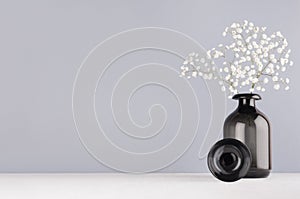 Simple minimalist spring interior in monochrome grey color - black glass circle and vase and bouquet of small white flowers.