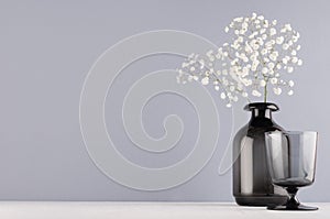 Simple minimalist spring interior in monochrome grey color - black glass drink and vase and bouquet of small flowers on white.