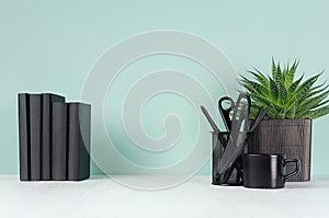 Simple minimalistic office interior with black stationery, books, coffee cup, aloe plant in pot in elegant green mint menthe.