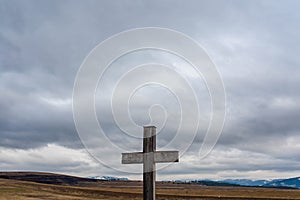 Simple oak catholic cross on focus, dramatic storm clouds, blue mountains with snow