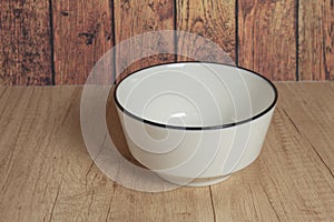 A simple picture of an empty white bowl on a rustic wooden table bathed in natural light