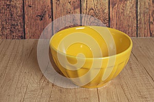 A simple picture of an empty yellow bowl on a rustic wooden table bathed in natural light
